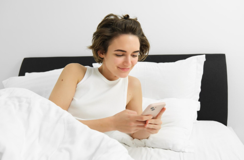 Woman checking her phone in bed after waking, reflecting why people google dreams.
